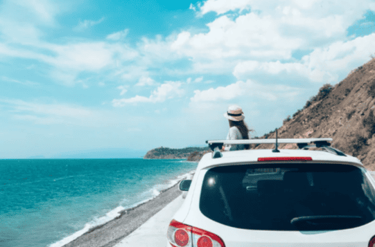 Lady in front of a car next to the ocean.
